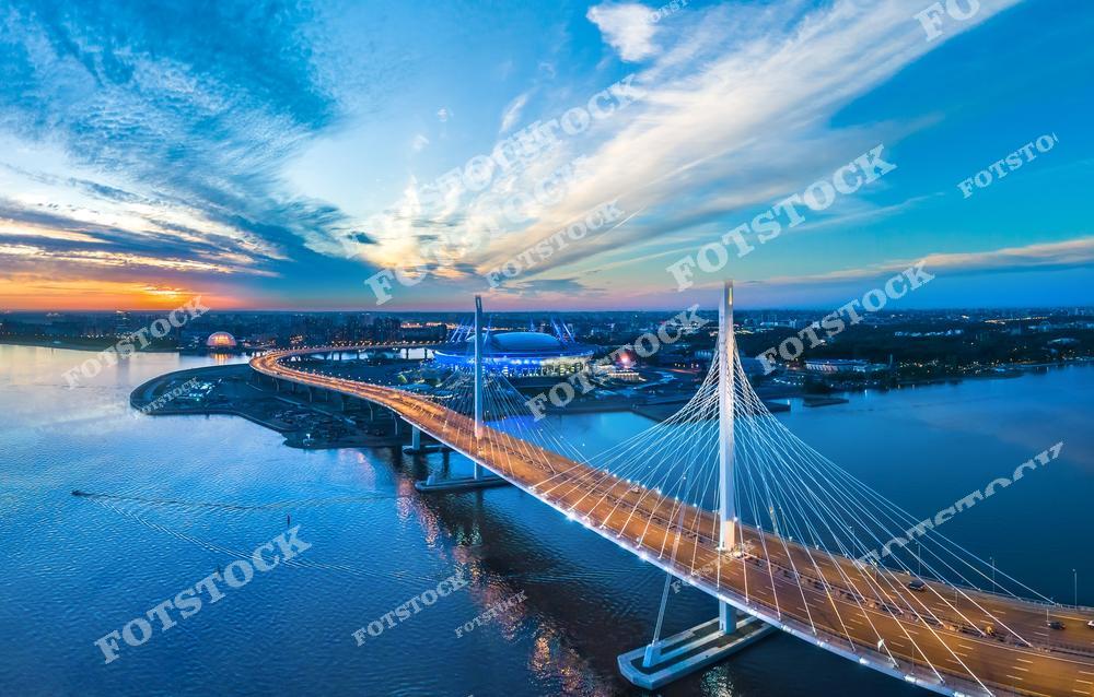 Панорамная фотография Санкт-Петербурга с высоты птичьего полета, на которой запечатлены современные магистрали, мосты города и Крестовский остров. Съемка с дрона позволяет увидеть масштаб городской инфраструктуры, панораму улиц и архитектуру Северной столицы России. На снимке гармонично сочетаются транспортные развязки, водные пространства и современные городские объекты, создавая динамичный городской пейзаж. Фотография передает атмосферу современного Петербурга и отлично подходит для туристических публикаций, фотостоков, рекламы, оформления интерьеров и материалов о городской архитектуре и транспорте.